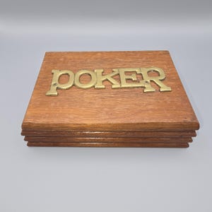 May include: A wooden box with the word "POKER" in gold-colored metal letters. The box is made of a light brown wood and has a stacked design. The letters are attached to the top of the box.