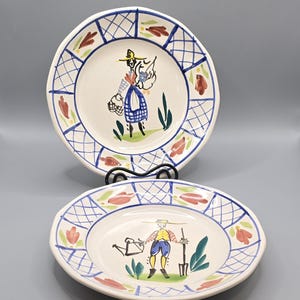 May include: Two decorative ceramic plates with hand-painted illustrations. The plates feature a white base with blue and red floral and geometric patterns around the rim. One plate depicts a person with a basket, the other a person with a watering can.