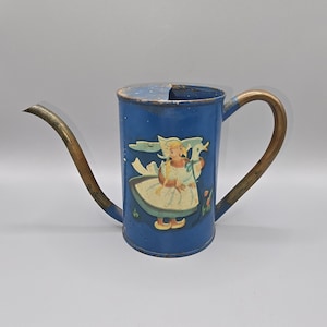 May include: Vintage blue metal watering can with a long spout and a curved handle. The can features a decorative image of a girl in a Dutch outfit. The spout and handle have a brass finish. A charming piece for garden decor.