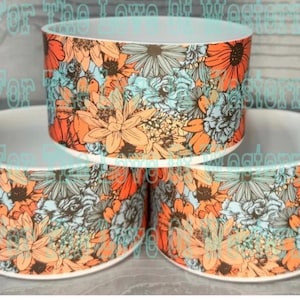 May include: Three ceramic bowls with a floral pattern. The design features orange, blue, and white flowers. The bowls are stacked, showcasing the colorful pattern. The bowls are likely for home decor or serving.