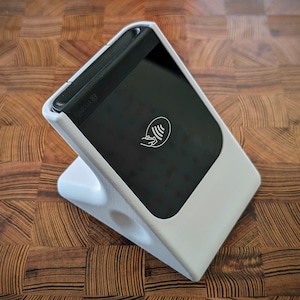 May include: White plastic stand with a black square device that says "Square 13" on the side. The device has a black screen with a white contactless payment symbol.