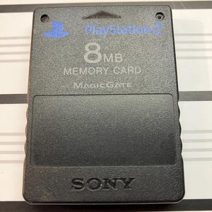May include: Black PlayStation 2 memory card with the text "PlayStation 2", "8 MB Memory Card", and "MagicGate" printed on it. The card also has the Sony logo printed on it.