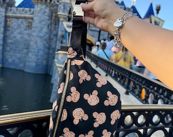 May include: A black belt bag featuring an all-over print of peach-colored Mickey Mouse-shaped pumpkins with green stems. The bag has a gold-tone zipper closure and a black adjustable strap with a gold-tone metal buckle.