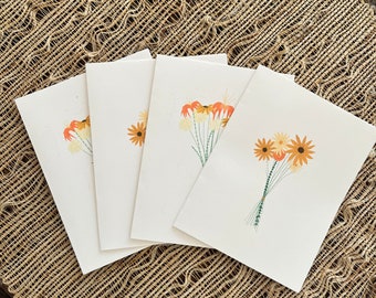 Könnte beinhalten: Vier leere Grußkarten mit einem handgemalten Blumendesign mit orangefarbenen, gelben und grünen Blumen. Die Karten sind übereinander gestapelt.