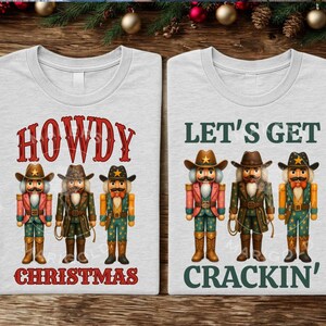 Pode incluir: Duas camisetas cinza claro com desenhos de quebra-nozes de cowboy. Uma camiseta diz "HOWDY CHRISTMAS" e a outra "LET'S GET CRACKIN'". Os quebra-nozes usam chapéus, jaquetas e botas de cowboy.