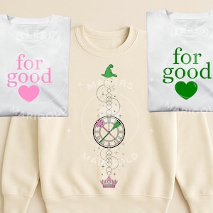 Op de afbeelding: Drie sweatshirts. Twee witte sweatshirts met de woorden "for good" en een hartafbeelding. Eén heeft een roze hart, de andere een groen hart. Het derde sweatshirt is beige met een klokontwerp, een heksenhoed en een kroon.