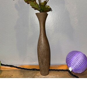 May include: A dark brown wooden vase with a narrow neck and a wide base, holding a bouquet of orange and yellow artificial flowers.