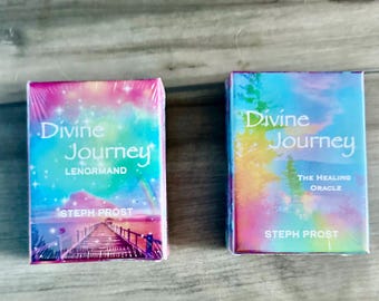 Könnte beinhalten: Zwei Orakelkarten-Decks mit dem Titel "Divine Journey" werden gezeigt. Eines ist mit "Lenormand" beschriftet, das andere mit "The Healing Oracle". Beide zeigen farbenfrohe, ätherische Kunstwerke und den Namen des Autors, Steph Prost.