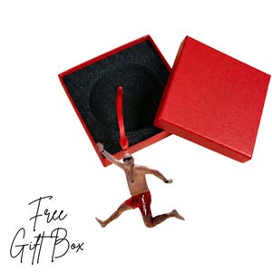 A man in red shorts is jumping out of a red gift box, with the box open and the man's arms raised.