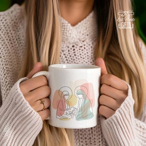 May include: White ceramic mug featuring a line art illustration of the Nativity scene with Mary, Joseph, and baby Jesus. The design includes pastel color blocks. The mug has a handle and the text "Last Minute GIFTS" is visible.