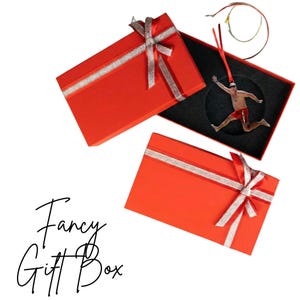 two red gift boxes with silver ribbons, one open and one closed, along with a small figure of a person in a red outfit.
