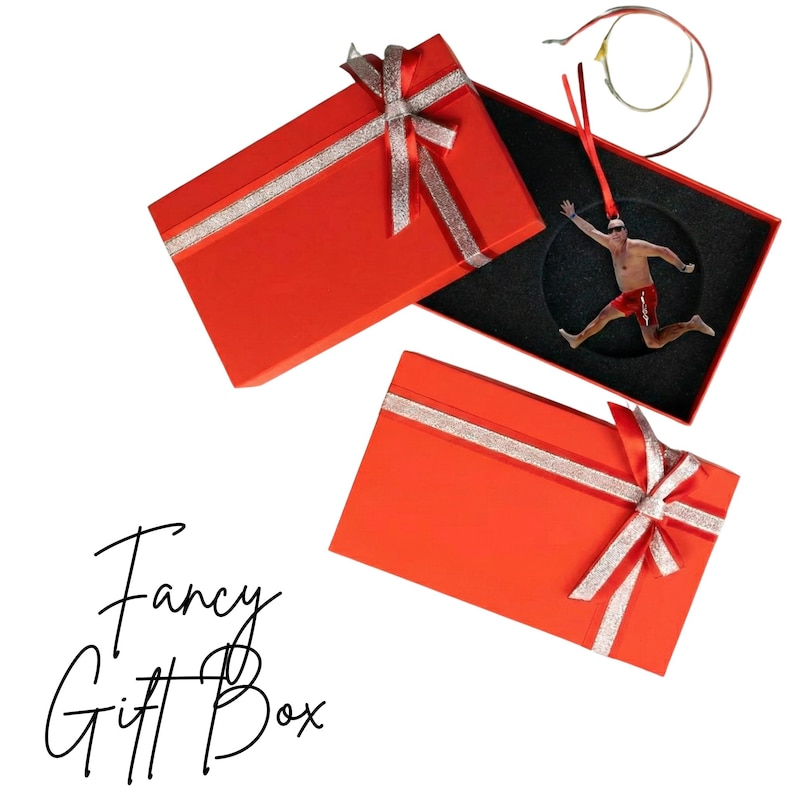 two red gift boxes with silver ribbons, one open and one closed, along with a small figure of a person in a red outfit.
