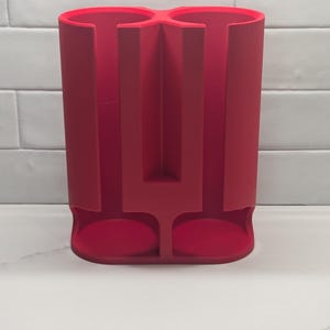 Peut inclure: Un porte-gobelets double en silicone rouge. Le porte-gobelets a deux compartiments séparés pour les gobelets et un séparateur central.