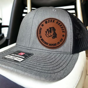 May include: A gray and black trucker hat with a brown leather patch that says "Work Harder People on Welfare Depend on You" with a pointing finger graphic.