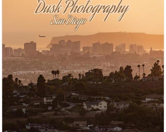 May include: A calendar featuring a photograph of San Diego at dusk. The image shows a cityscape with buildings, trees, and a plane in the sky, all bathed in warm orange and yellow hues. The text "Dusk Photography San Diego" is at the top.