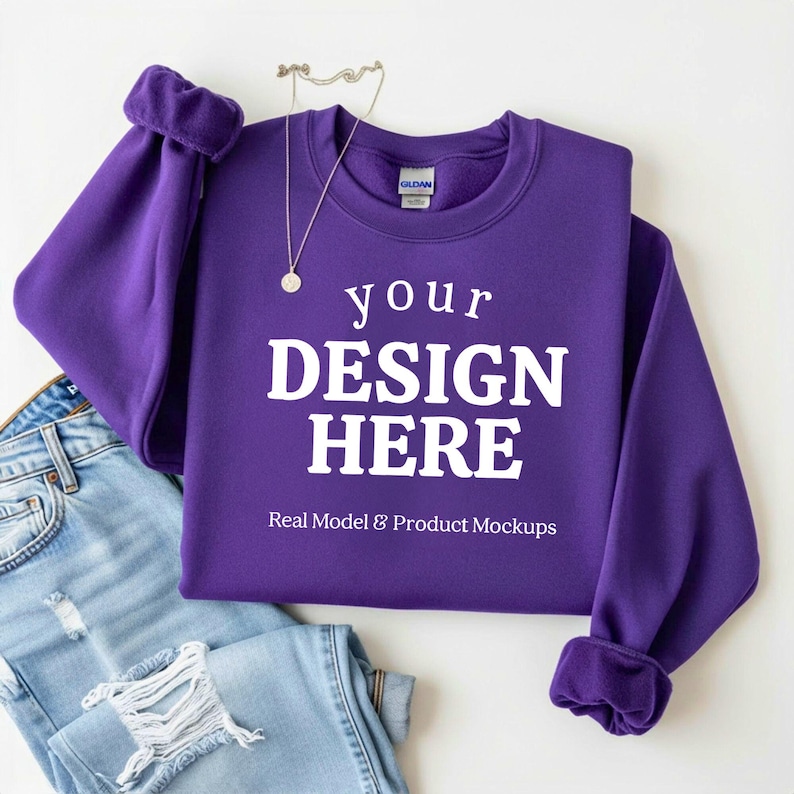 May include: A purple sweatshirt with the text "your DESIGN HERE" in white, with a pair of blue jeans and a silver necklace. The sweatshirt is a mock-up for design placement. The text "Real Model & Product Mockups" is also visible.