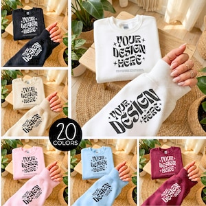 Może przedstawiać: Makieta prezentująca różne bluzy z okrągłym dekoltem w różnych kolorach, w tym czarnym, białym, beżowym, różowym, jasnoniebieskim i bordowym. Każda bluza ma napis "YOUR DESIGN HERE" w stylu retro. Obraz przedstawia 20 opcji kolorystycznych.