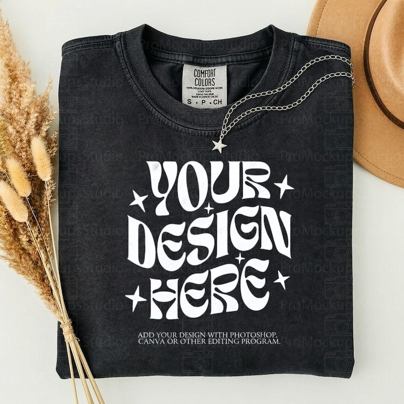 May include: Black t-shirt with the text "YOUR DESIGN HERE" in white, with star accents. A silver necklace with a star pendant and a brown hat are also visible. The shirt has a Comfort Colors tag.