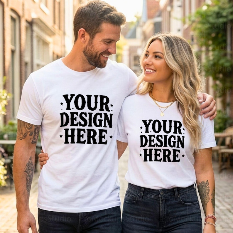 May include: Two people wearing white t-shirts with the text "YOUR DESIGN HERE" in black. The shirts are short-sleeved and the text is centered. The people are smiling and appear to be in an outdoor setting.