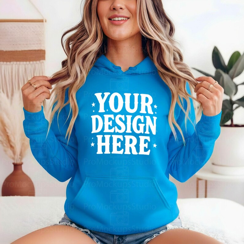 K&ouml;nnte beinhalten: Ein leuchtend blauer Kapuzenpullover mit dem wei&szlig;en Text "YOUR DESIGN HERE", mit einer K&auml;ngurutasche und einer Kapuze. Der Kapuzenpullover wird von einer Person getragen.
