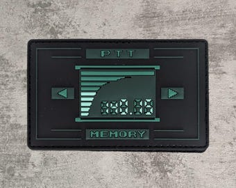 Puede incluir: Un parche rectangular negro con un gráfico de pantalla digital verde. El diseño incluye el texto PTT en la parte superior y MEMORY en la parte inferior, con un gráfico de barras pixelado, flechas direccionales y una lectura numérica en el centro.