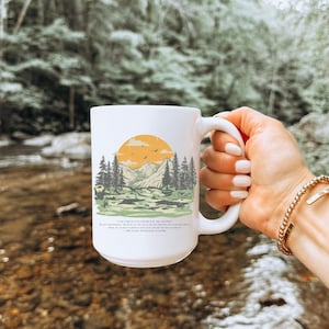 Peut inclure: Une tasse en céramique blanche avec une scène de montagne et un graphique de coucher de soleil. Le texte sur la tasse est "Où que tu ailles, va-y de tout ton cœur."