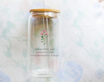 Puede incluir: Un tarro de vidrio transparente con tapa de bambú y una pajita. El tarro tiene una ilustración de una flor rosa y el texto "completely and perfectly and incandescently happy".