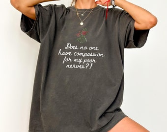 May include: A dark gray oversized t-shirt with a white graphic that reads "Does no one have compassion for my poor nerves?!" with a small red floral design above the text.