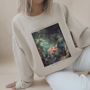 May include: A beige sweatshirt featuring a print of a painting by Jean-Honoré Fragonard titled "The Swing, 1767".