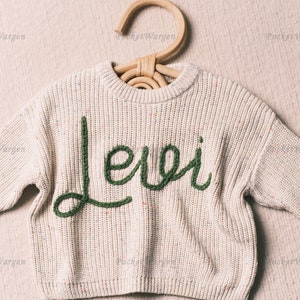 May include: A cream-colored knitted sweater with a green embroidered name "Levi" on the front.