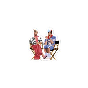 May include: Two people sitting in director's chairs. The person on the left is wearing a striped shirt, pink pants, and a hat. The person on the right is wearing a blue jersey with the number 57, a red scarf, and a blue hat.