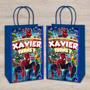 May include: Two dark blue paper gift bags featuring a Spider-Man graphic, a city background, and the text "THANK YOU FOR COMING TO CELEBRATE XAVIER TURNS 7". The bags have dark blue handles and a vertical blue glitter border on each side of the central image.