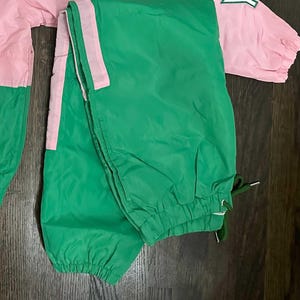 May include: Green and pink nylon tracksuit with a white stripe down the side of the legs. The tracksuit is folded in half.