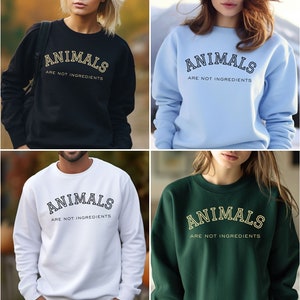 May include: A collection of eight crewneck sweatshirts in various colors, each displaying the text "ANIMALS ARE NOT INGREDIENTS" in a collegiate-style font. The sweatshirts are in shades of beige, black, light blue, gray, navy, white, green, and pink.