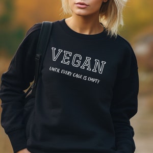 May include: Black sweatshirt with white text that reads "VEGAN UNTIL EVERY CAGE IS EMPTY".
