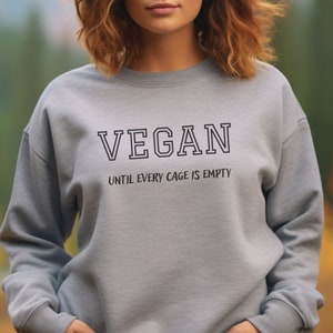 May include: Gray sweatshirt with the text "VEGAN" in black outlined letters and the text "UNTIL EVERY CAGE IS EMPTY" in smaller black letters below.
