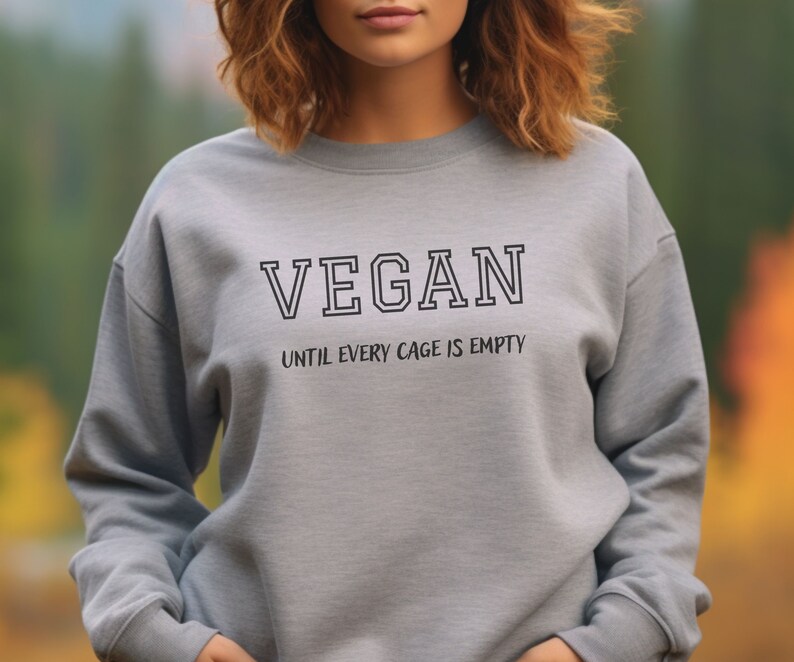 May include: Gray sweatshirt with the text "VEGAN" in black outlined letters and the text "UNTIL EVERY CAGE IS EMPTY" in smaller black letters below.