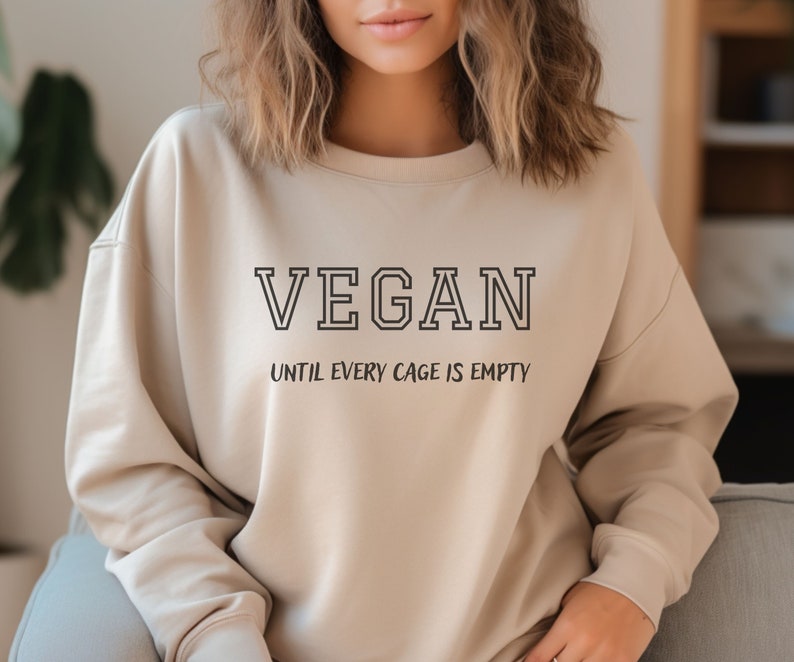 May include: A beige sweatshirt with the text "VEGAN UNTIL EVERY CAGE IS EMPTY" printed on the front.