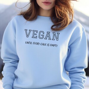 May include: A light blue sweatshirt with the text "VEGAN UNTIL EVERY CAGE IS EMPTY" printed on the front.