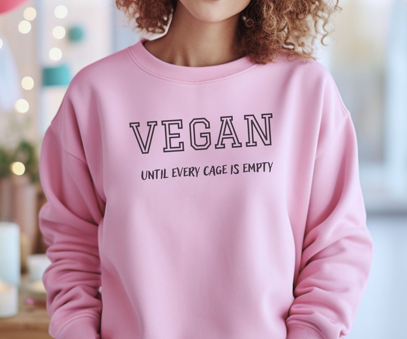 May include: Pink sweatshirt with the text "VEGAN UNTIL EVERY CAGE IS EMPTY" printed on the front.