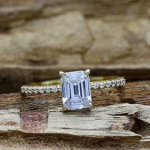May include: A gold ring with a large, clear emerald-cut diamond and a band of smaller diamonds.