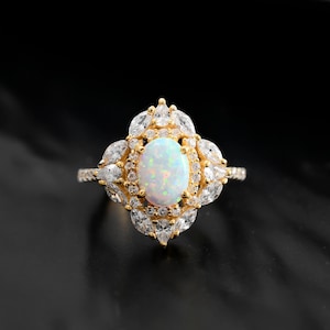 Può includere: Un anello d'oro con un grande opale ovale circondato da pietre più piccole e trasparenti.