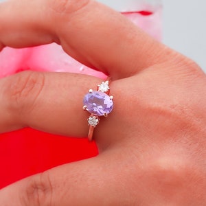 May include: A hand wearing a ring with a large oval amethyst gemstone and smaller diamond accents. The ring is set in rose gold.