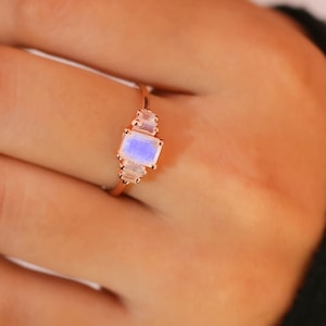 Puede incluir: Un anillo de oro rosa con una gran piedra de luna rectangular y pequeños acentos de piedra de luna.