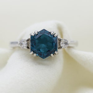 May include: A silver ring with a large, hexagonal, dark blue gemstone surrounded by smaller, clear gemstones.