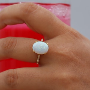 May include: A gold ring with a white oval opal gemstone. The ring is set with small diamonds around the opal.