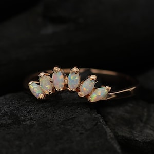 May include: A delicate rose gold ring featuring a row of marquise-shaped opal stones. The stones are set in a curved line, creating a unique and elegant design.