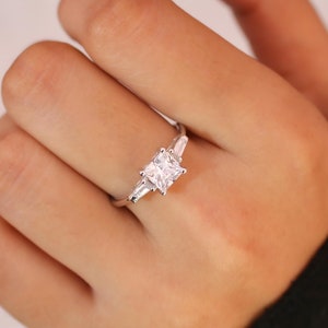 May include: A silver ring featuring a square-shaped centre stone and two smaller baguette-shaped stones on either side.