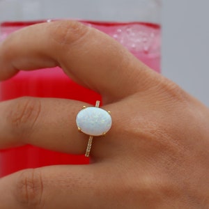 Könnte beinhalten: Ein goldener Ring mit einem weißen ovalen Opal-Edelstein, der in eine Diamant-Pave-Band gefasst ist.