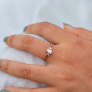 Könnte beinhalten: Ein Ring aus Roségold mit einem großen ovalen Diamanten und zwei kleineren runden Diamanten auf jeder Seite.